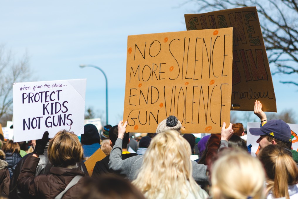 Protest signs read "Protect kids, not guns" and "No more silence, end gun violence"