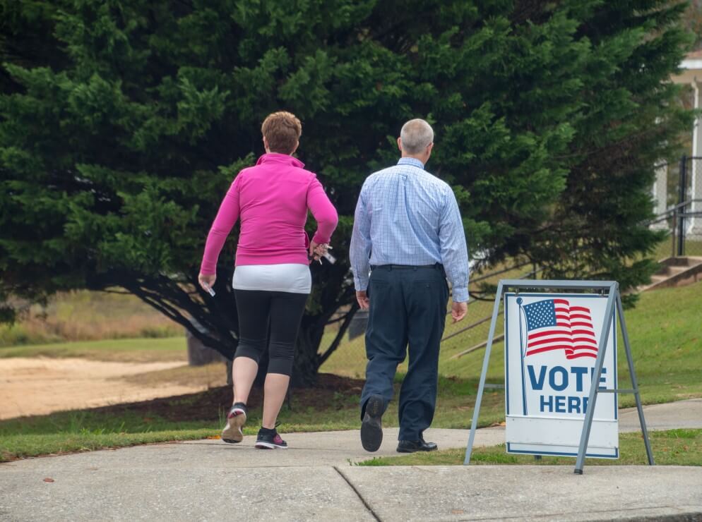 Two white people walk by "Vote" sign at polling location