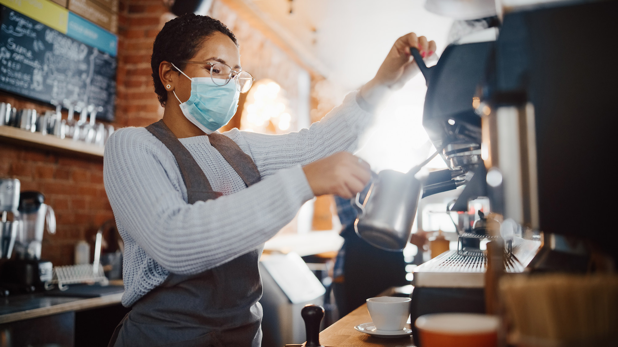 Barista wearing mask making latte in coffee shop