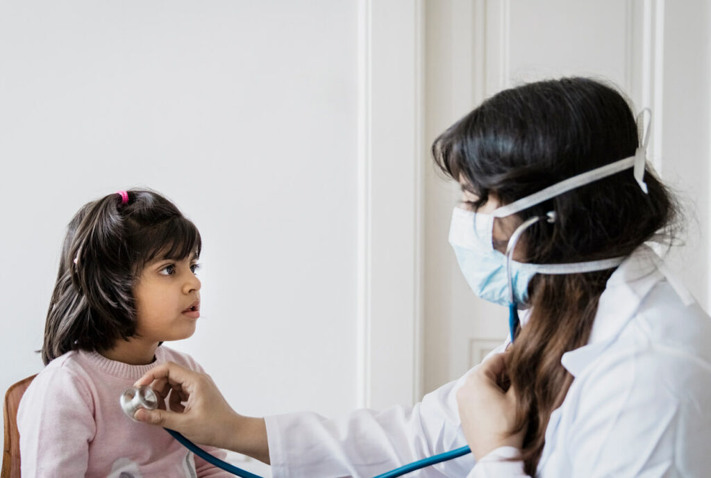 Girl looking at doctor examining with stethoscope