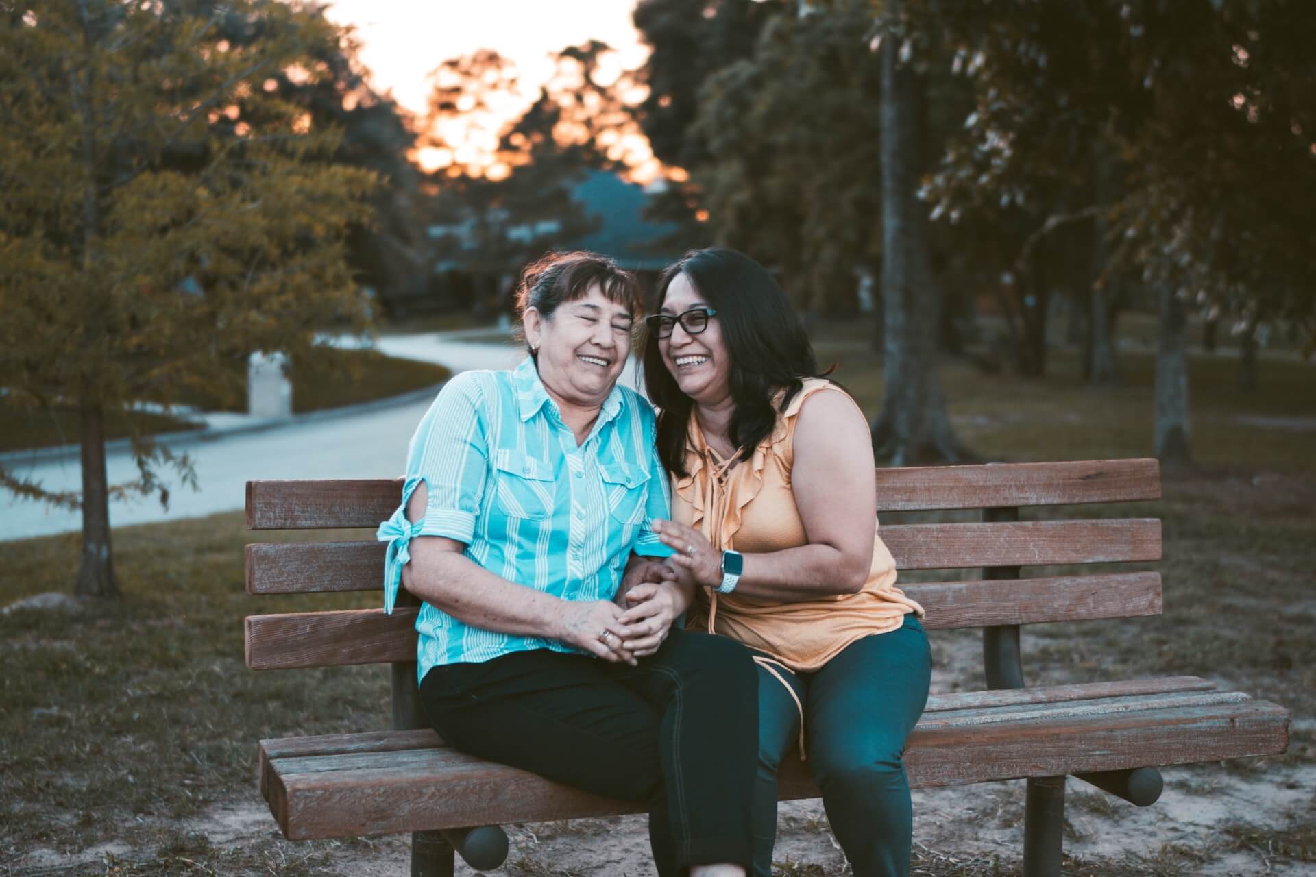 Two middle aged Latina women sit laughing on park bench Photo by Dario Valenzuela