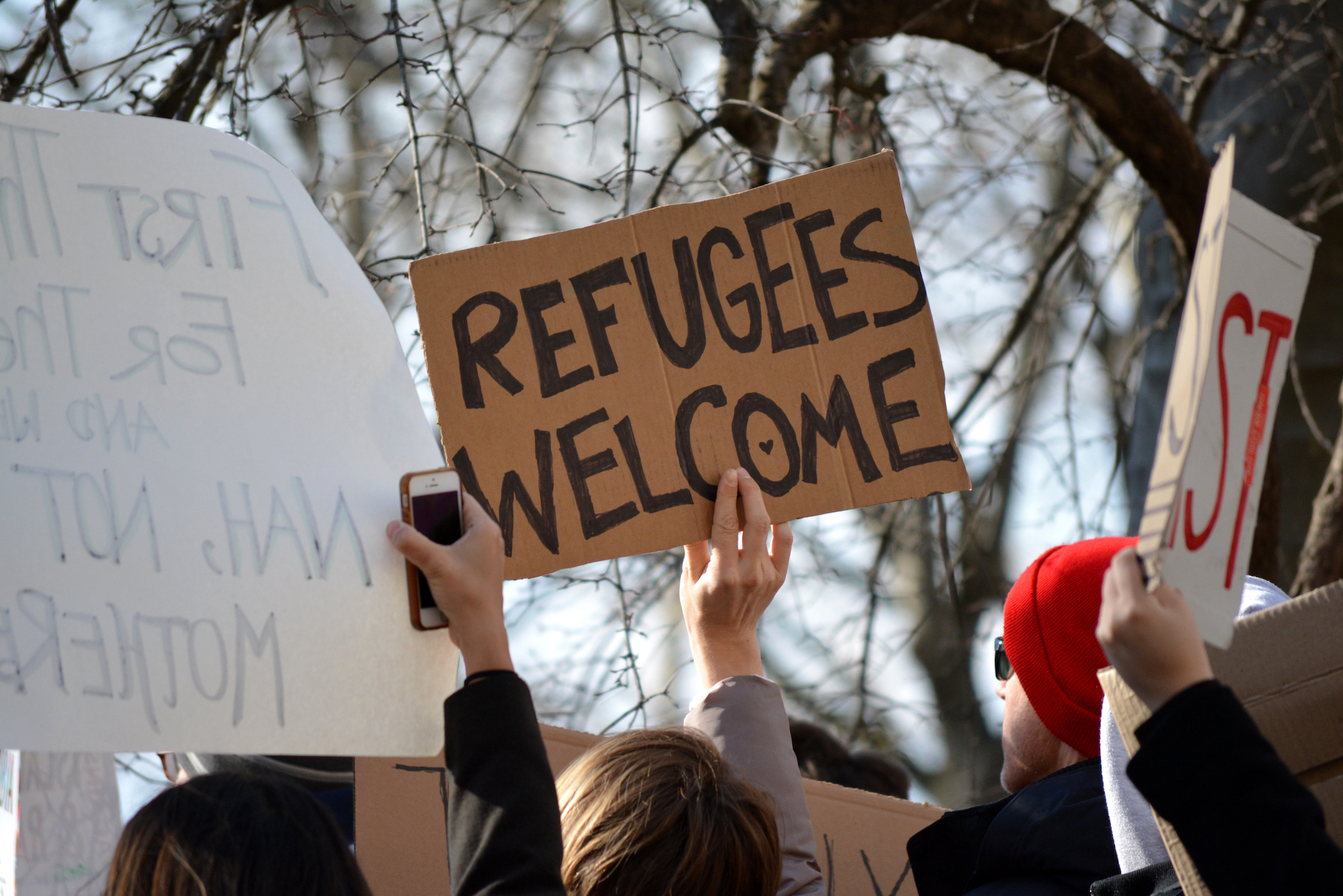 rally sign reads "Refugees Welcome"
